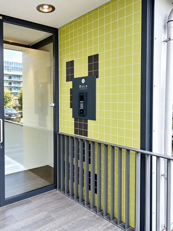 Entrance with a glass door next to a yellow tiled wall with the BoLo Workspaces doorbell